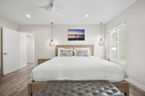 Relax in this serene bedroom with a large bed, wooden headboard, and a bench, surrounded by a large window and a beautiful painting.