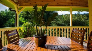 A covered outdoor seating area with a wooden table and chairs, surrounded by lush greenery. - The Garden Cottage, a traditional island home in the heart of Martinique (Gros-Morne)