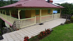 A two-story house with a red roof and a covered porch. - The Garden Cottage, a traditional island home in the heart of Martinique (Gros-Morne)