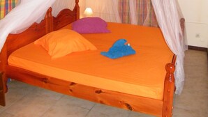 A bed with a wooden frame and an orange mattress, covered by a white canopy. - The Garden Cottage, a traditional island home in the heart of Martinique (Gros-Morne)