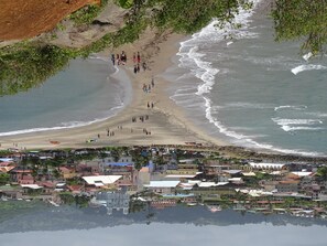A coastal town with a beach, buildings, and a reflection in the water.