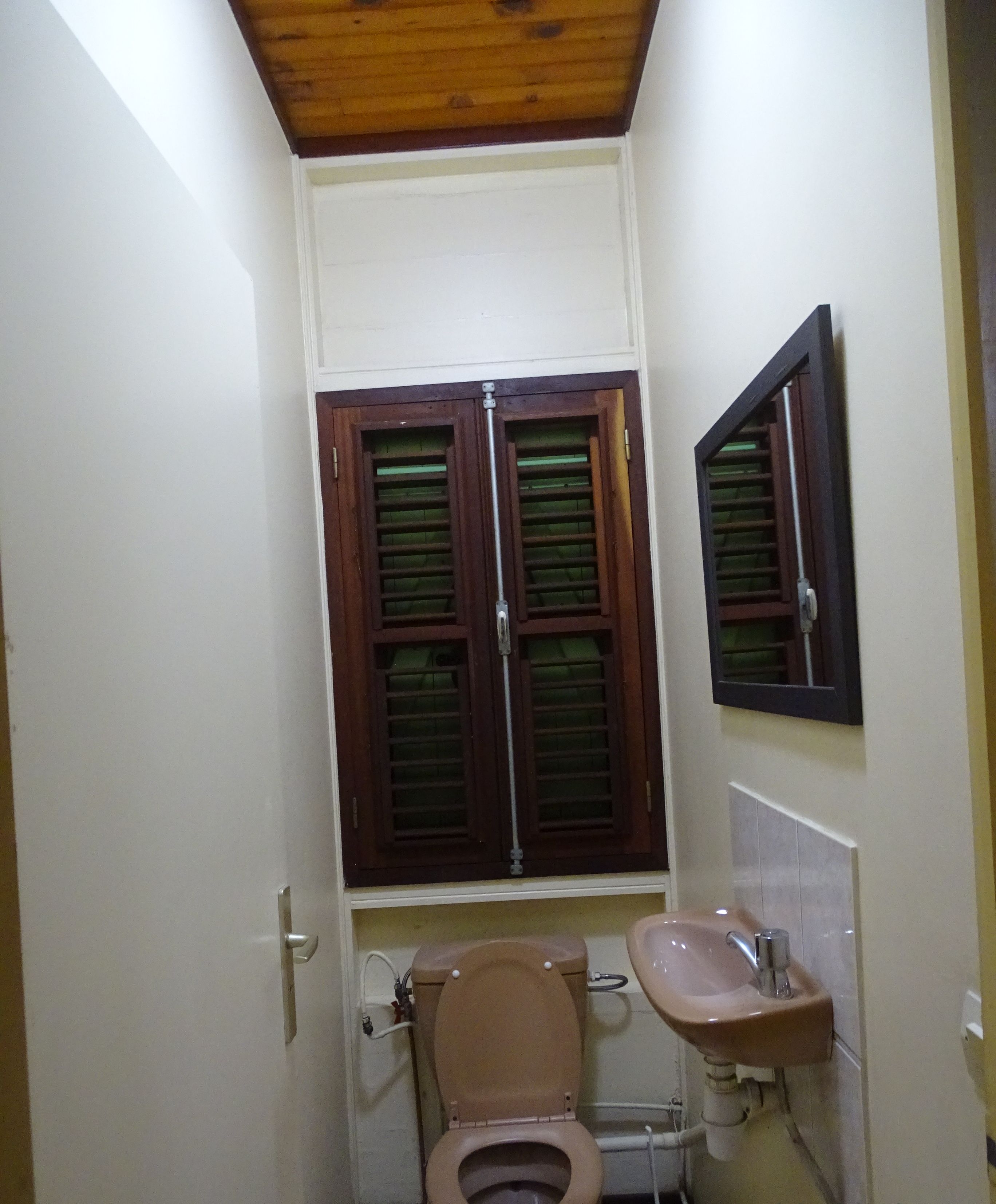 Un baño pequeño con inodoro, lavamanos y ventana con contraventanas.