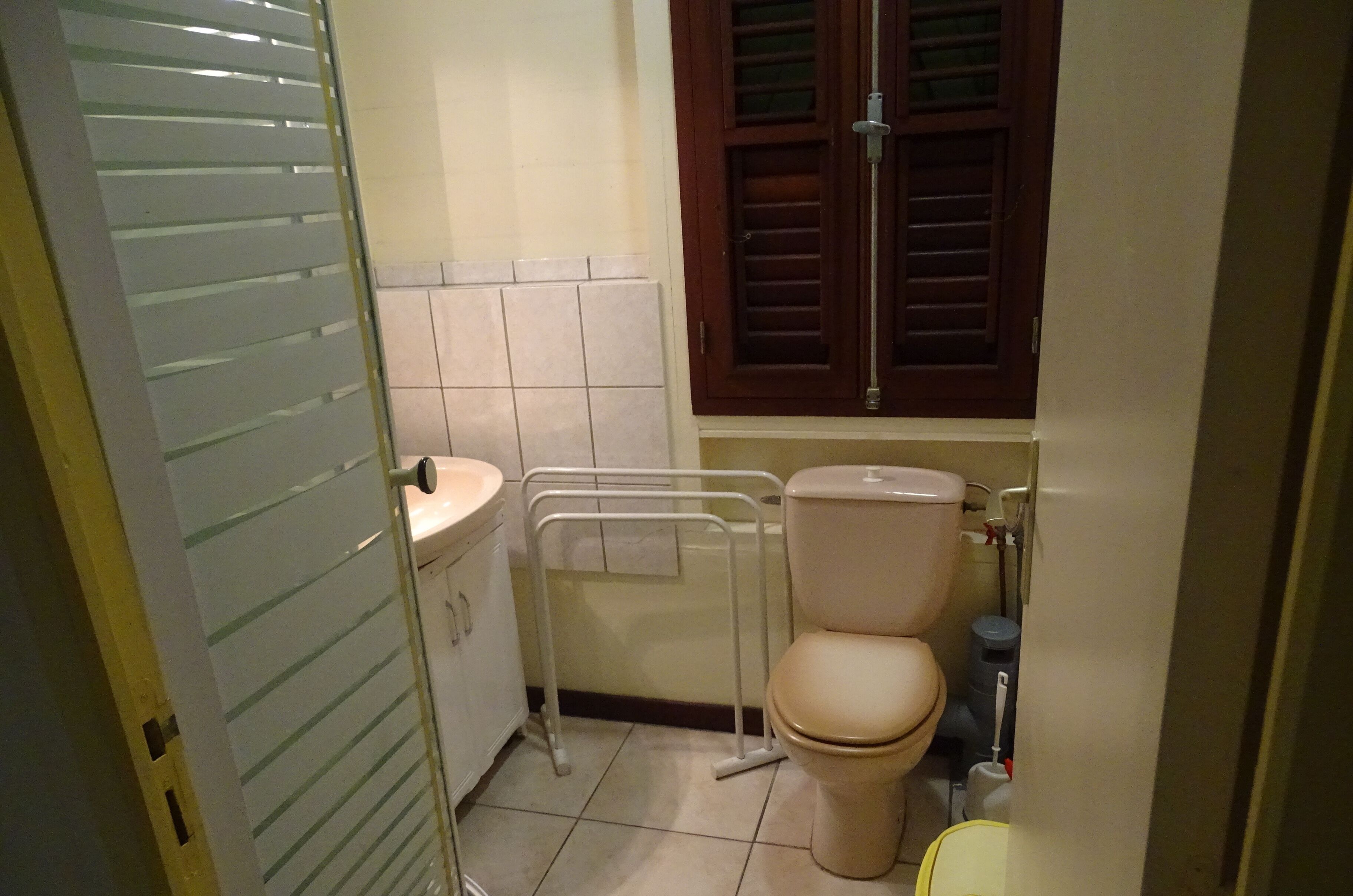 Un baño pequeño con inodoro, lavamanos y ventana con contraventanas de madera.