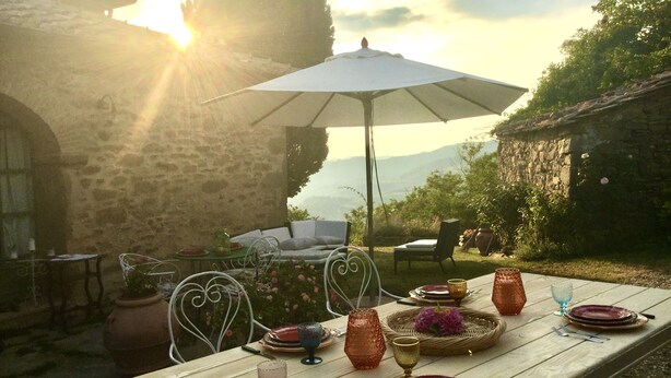 An outdoor dining area with a table set for a meal, surrounded by stone walls and a view of the mountains.