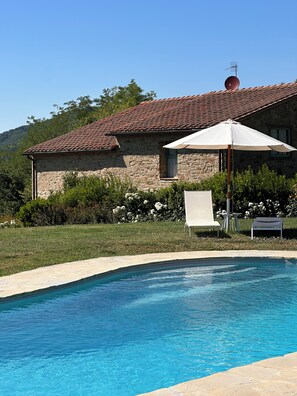 A stone building with a tiled roof, a swimming pool, and a white umbrella.