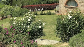 A stone building with a tiled roof, surrounded by well-maintained gardens with various flowering plants and a lawn.
