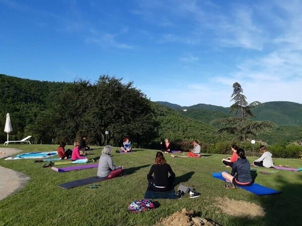 A group of people sitting on yoga mats outdoors with a scenic view of hills and trees in the background.