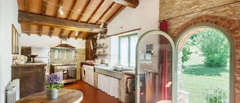 Cocina rústica con vigas de madera, lavadora y ventana grande con vista a un jardín.