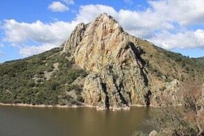 A mountain with a lake at its base, surrounded by greenery and rocky terrain.