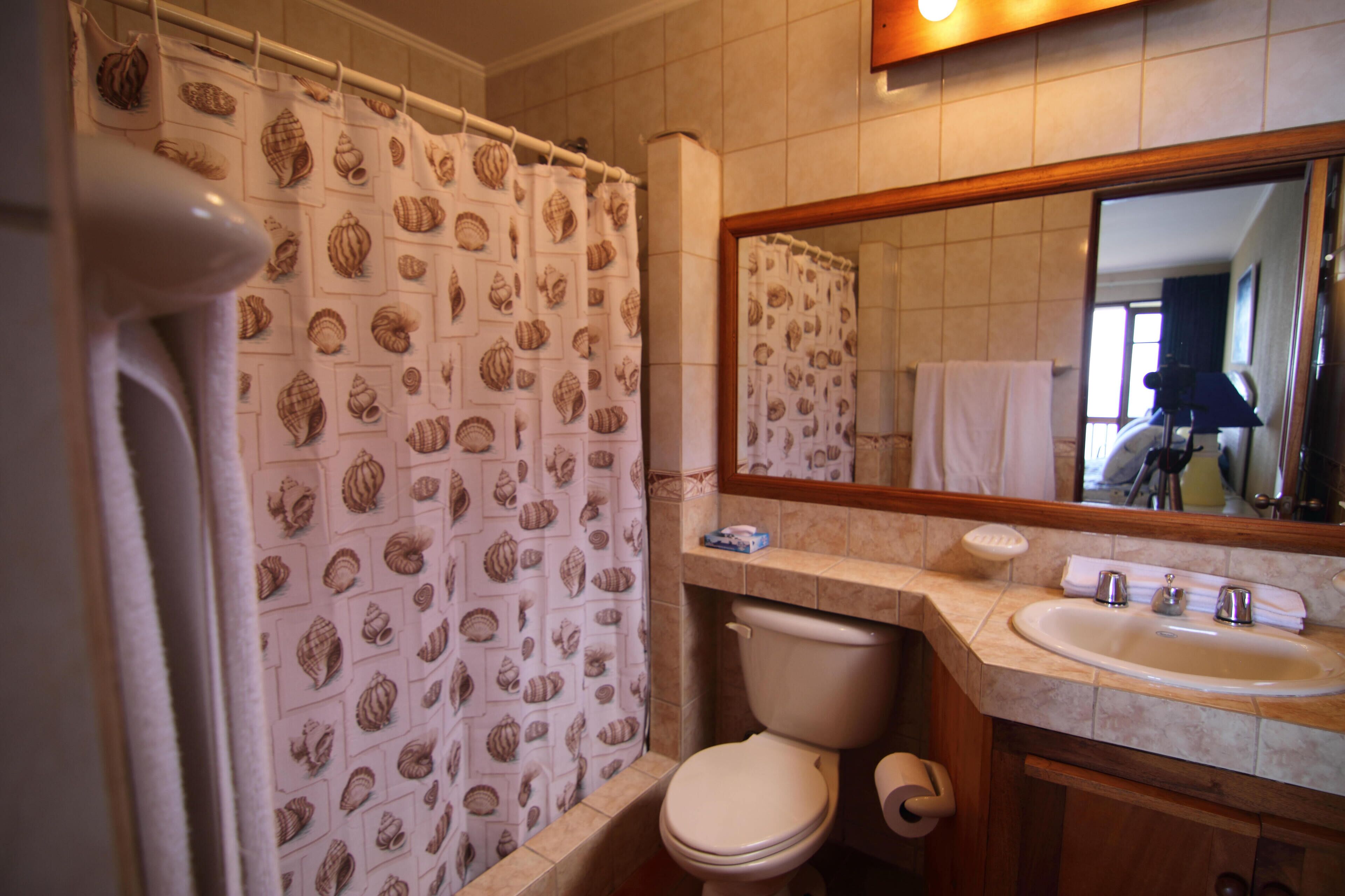 Een badkamer met toilet, wastafel en een douchegordijn met schelpenprint.