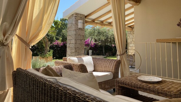 An outdoor seating area with wicker furniture, a stone pillar, and a view of the garden.