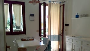A kitchen with a white table, chairs, a cabinet, and a window with curtains.
