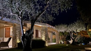 A well-lit outdoor area with stone pillars, a large tree, and a covered seating area.