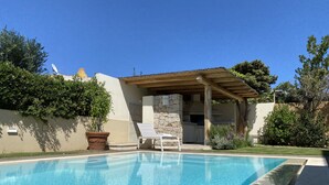 A swimming pool with a pergola and a stone barbecue area.