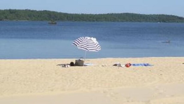 A beach with a striped umbrella, a boat, and a forest in the background. - House with private pool, in a quiet location close to Mimizan.  (Saint-Paul-en-Born)