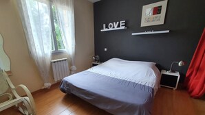 A bedroom with a bed, a nightstand, a wall-mounted shelf with a 'LOVE' sign, a radiator, and a window with sheer curtains. - House with private pool, in a quiet location close to Mimizan.  (Saint-Paul-en-Born)