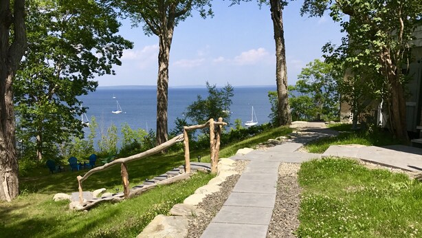 A stone pathway leading to a grassy area with trees and a view of the sea.