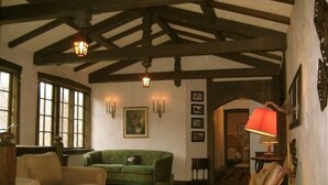 A room with a high ceiling, exposed wooden beams, a green sofa, a beige armchair, and a red lamp.