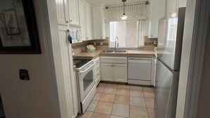 A kitchen with white cabinets, a stove, an oven, a dishwasher, a refrigerator, and a window with curtains. - +Front row condo. Steps to sandy beach, sunset,  trails. Exclusive Resort+ (Dana Point)