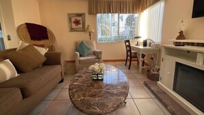 A living room with a brown sofa, a round marble coffee table, a wicker chair, a dining table, and a fireplace. - +Front row condo. Steps to sandy beach, sunset,  trails. Exclusive Resort+ (Dana Point)
