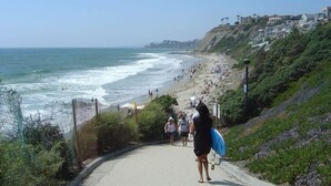 A coastal walkway with a beach in the background, leading to a cliff with houses. - +Front row condo. Steps to sandy beach, sunset,  trails. Exclusive Resort+ (Dana Point)