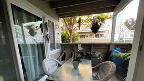 A covered patio area with a glass table and wicker chairs, a potted orchid, and a hanging basket with flowers. - +Front row condo. Steps to sandy beach, sunset,  trails. Exclusive Resort+ (Dana Point)