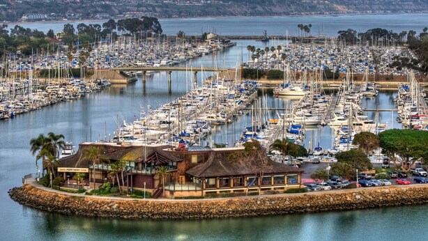A marina with numerous boats docked, a prominent building labeled 'DANA POINT YACHT CLUB', and a bridge connecting the marina to the land. - +Front row condo. Steps to sandy beach, sunset,  trails. Exclusive Resort+ (Dana Point)