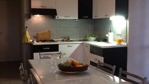 A modern kitchen with white and dark cabinets, a stainless steel sink, and a dining table set with a fruit bowl and glasses. - House PANORAMIC VIEW SEA between SEA and MOUNTAIN  (Nocera terinese)