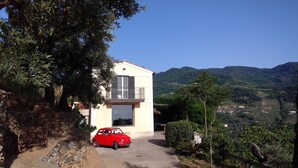 A two-story building with a balcony, a red car parked in front, and a view of a hilly landscape. - House PANORAMIC VIEW SEA between SEA and MOUNTAIN  (Nocera terinese)
