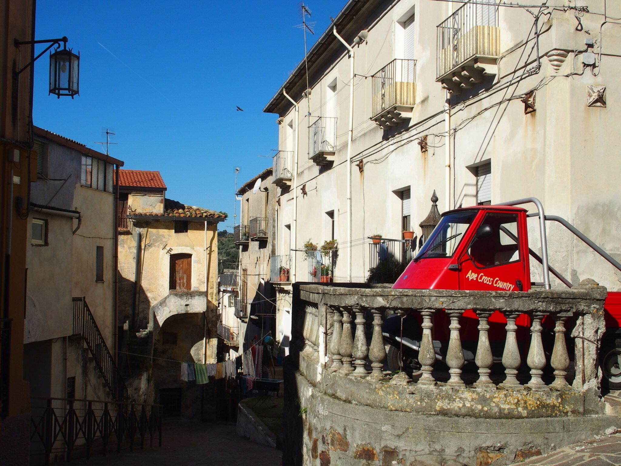 A narrow street with buildings, a red truck, and a stone balustrade.