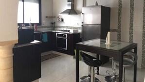 A modern kitchen with a gas stove, oven, and refrigerator. There is a dining table with chairs and a hanging light fixture.
