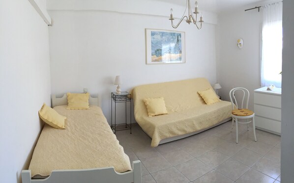A bedroom with two beds, a chair, a nightstand, a lamp, a painting, and a window with curtains.