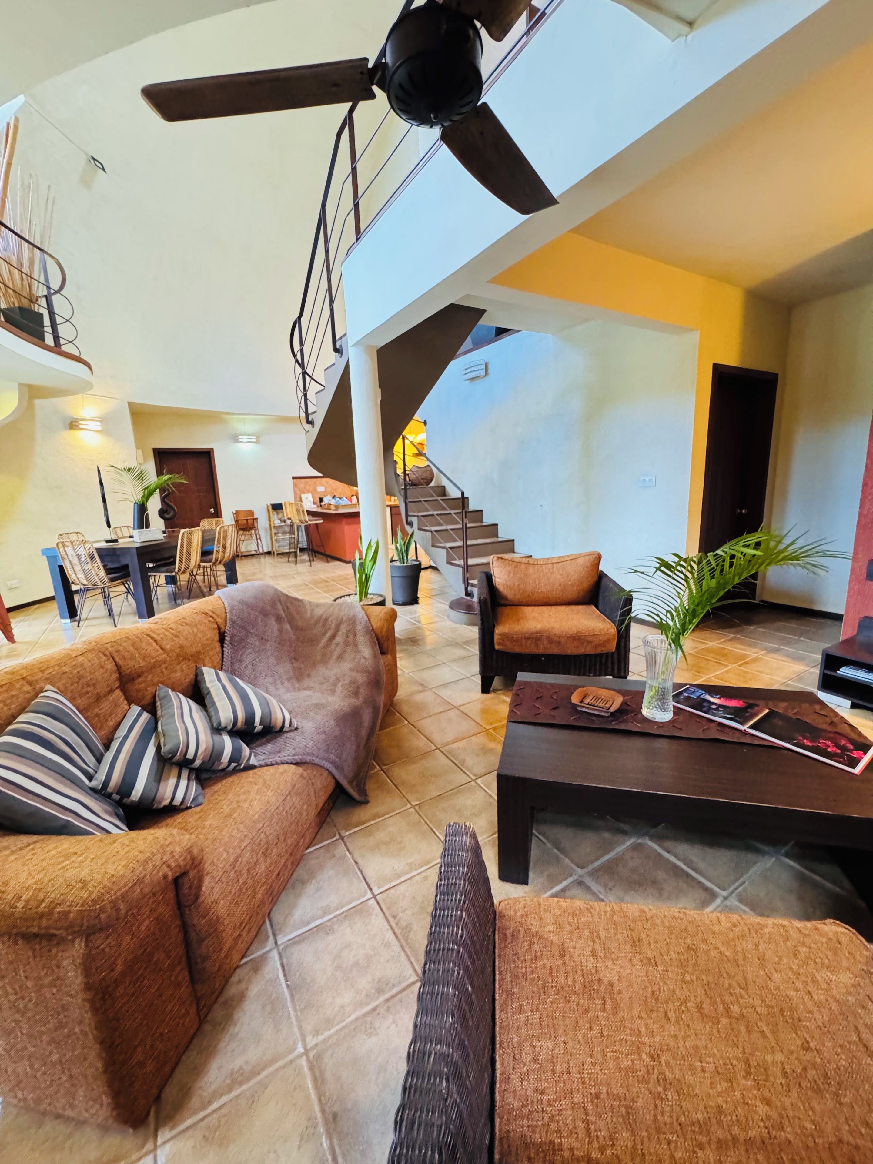 A spacious living area with a sofa, armchairs, a coffee table, and a ceiling fan. A staircase leads to an upper level.