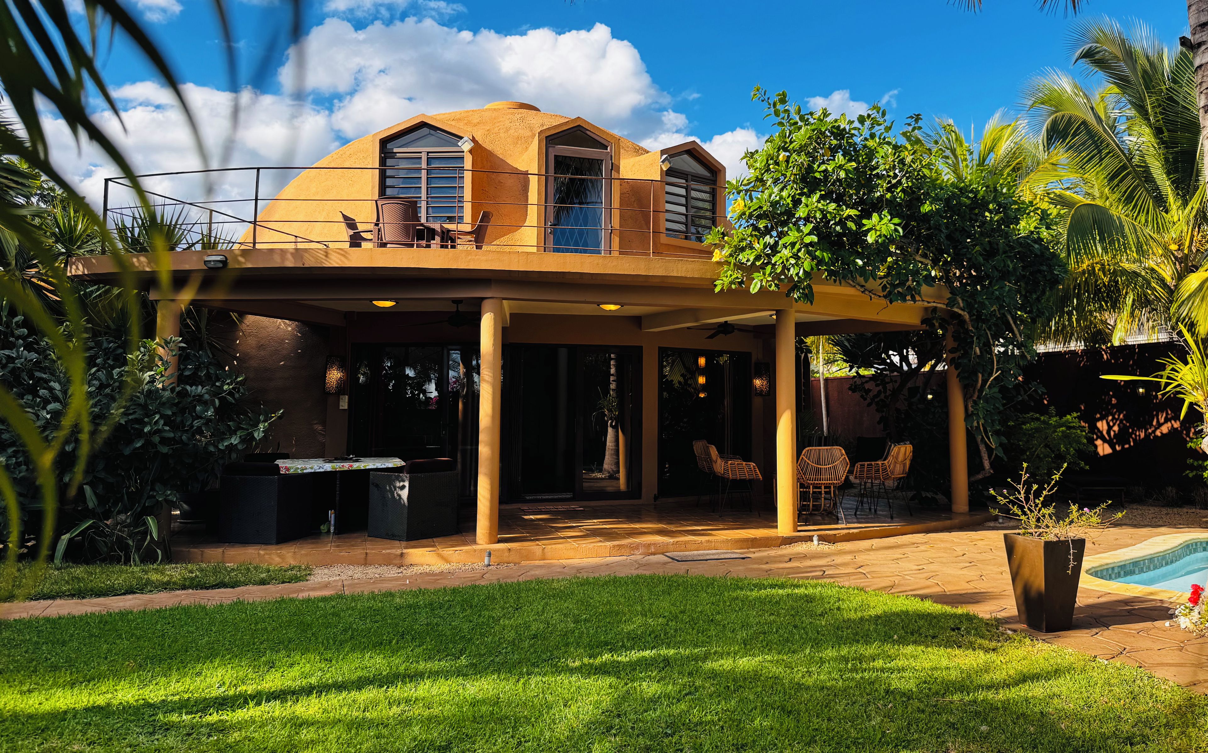 Una casa con veranda coperta, piscina e vegetazione rigogliosa.