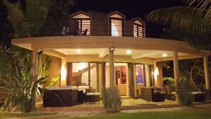 Une maison à deux étages dotée d’un patio couvert, aménagé avec du mobilier d’extérieur et offrant un intérieur bien éclairé.