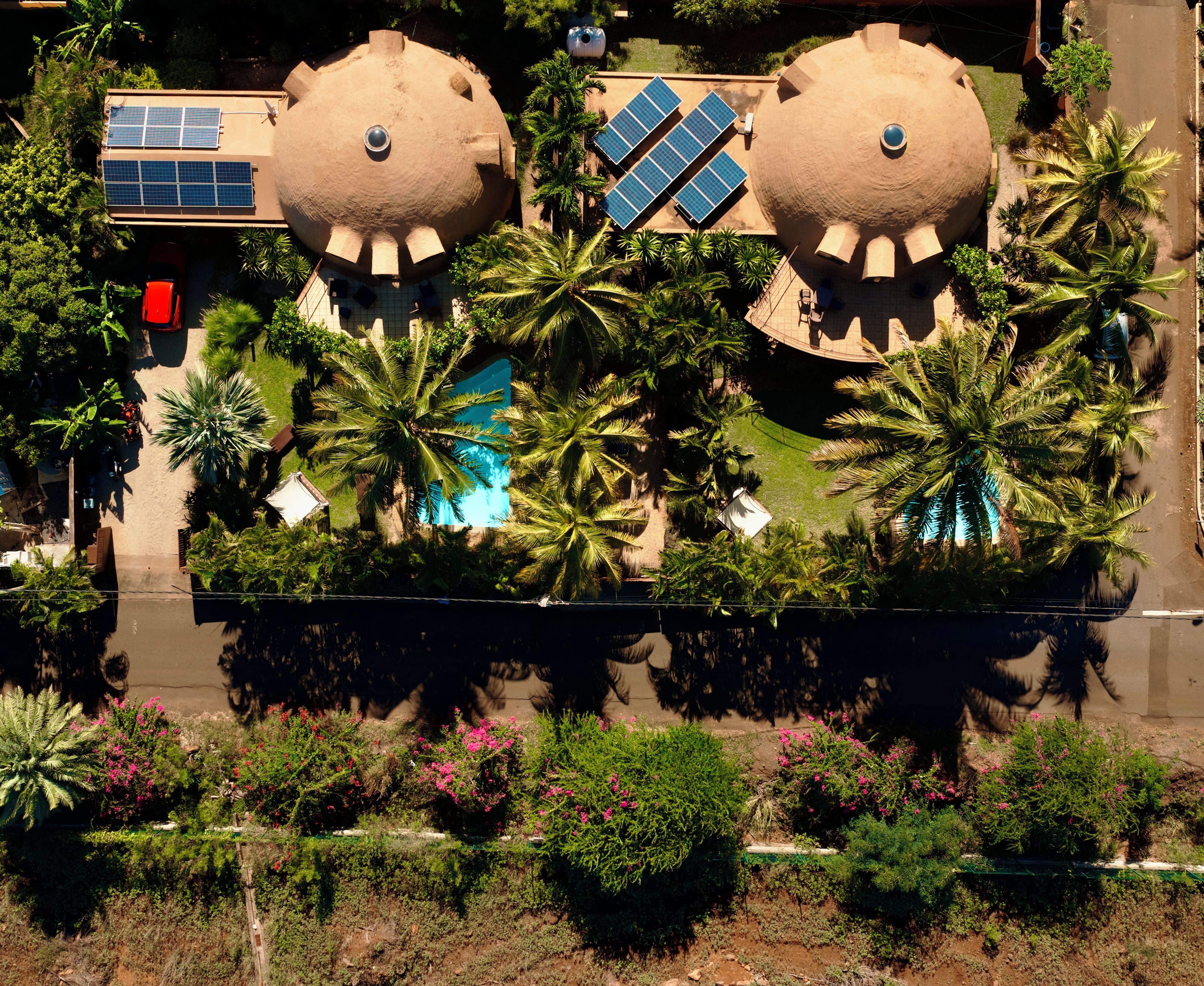 A large building with two spherical structures, solar panels, a swimming pool, and surrounding palm trees.