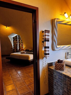 A hotel room with a bed, a bathroom with a sink and mirror, and a wall-mounted telephone.