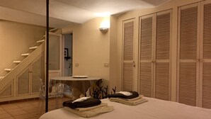 Un dormitorio con cama, escritorio y silla. Se ve una escalera que lleva a otra habitación.