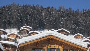 Una cabaña de madera con varios balcones y ventanas, rodeada de árboles nevados y un cielo despejado.