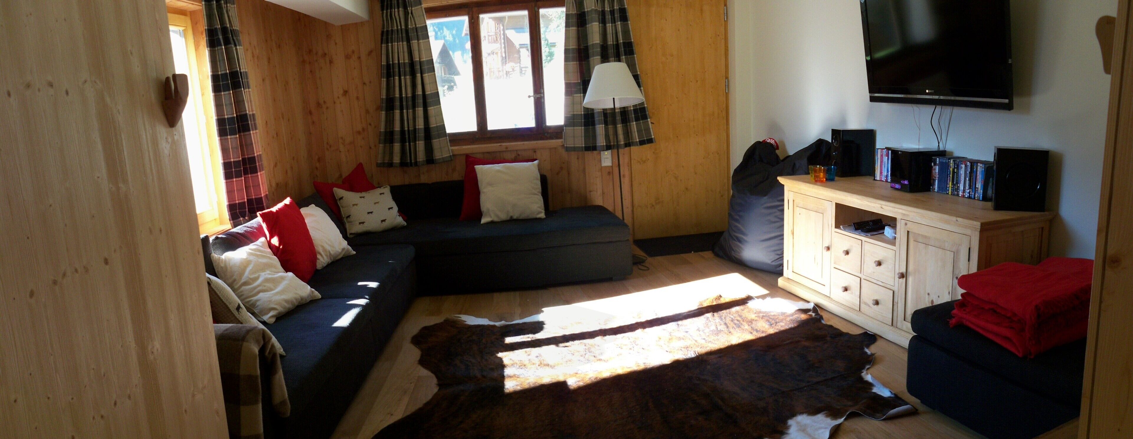 A cozy room with a sectional sofa, a wooden cabinet with media, and a large window with plaid curtains.