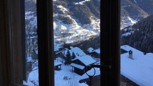 Vista de un paisaje montañoso cubierto de nieve a través de una ventana con marcos de madera.