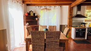 Un comedor con mesa de madera y sillas de mimbre, techo con vigas a la vista, y una zona de cocina con estufa y armarios.