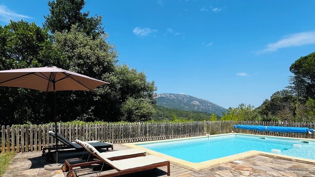 Un patio de piedra con piscina, sillas de descanso y una sombrilla.