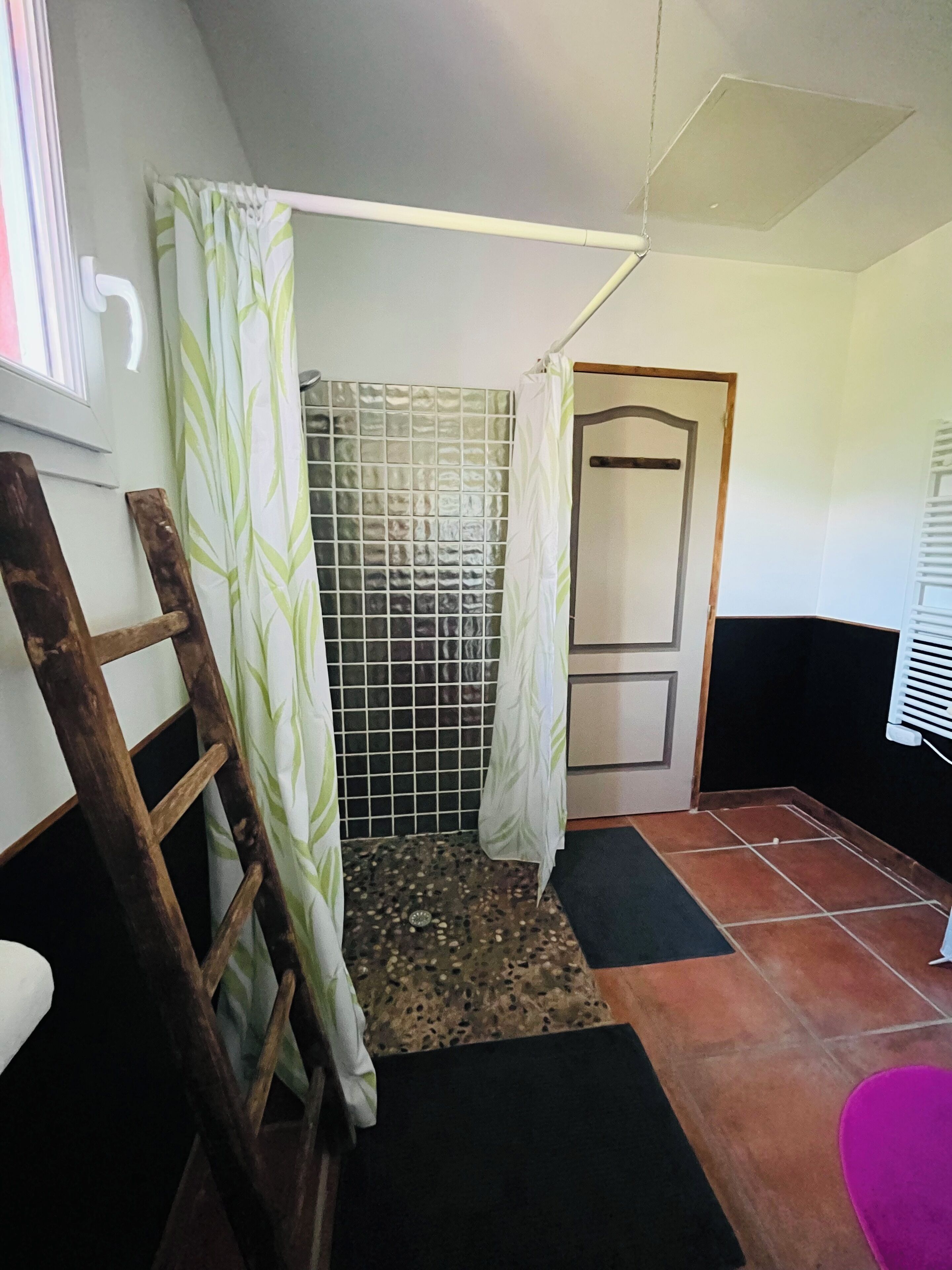 Un bagno con doccia, una scala di legno, pavimento piastrellato e una porta.