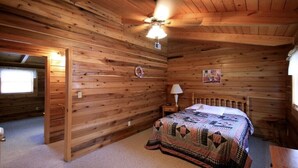 A wooden cabin bedroom with a bed, a nightstand, a ceiling fan, and a window. - Valley View Cabin with show-stopping vaulted ceilings!  (Hico)