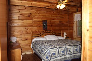 Une chambre rustique en bois, avec un lit, une table de chevet, un ventilateur de plafond et un panneau accroché au mur.