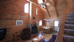 A log cabin interior with a fireplace, a dining area, a sofa, and a staircase. - Valley View Cabin with show-stopping vaulted ceilings!  (Hico)