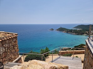 Une vue sur la côte, avec un escalier en pierre descendant vers la plage, surplombant la mer et une petite colline surmontée d’une tour.