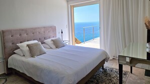 A bedroom with a large bed, a nightstand, a chair, and a view of the sea through a balcony. - Luxury villa 5 * panoramic sea view private heated pool + SPA (Conca)