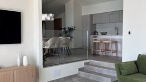 A modern living room with a green sofa, a coffee table, and a TV mounted on the wall. There is a staircase leading to a dining area with a table and chairs. - Luxury villa 5 * panoramic sea view private heated pool + SPA (Conca)